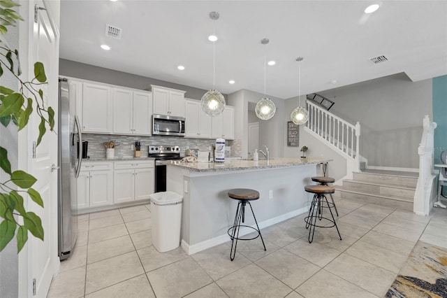 720 Gardenia Ln, Davenport, FL 33897 - kitchen featuring appliances with stainless steel finishes, light tile patterned floors, tasteful backsplash, white cabinetry, and a kitchen island with sink