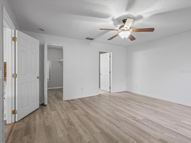 112 Lake Butler Ave, Haines City, FL 33844 - unfurnished bedroom with light wood finished floors, a spacious closet, baseboards, a textured ceiling, and ceiling fan