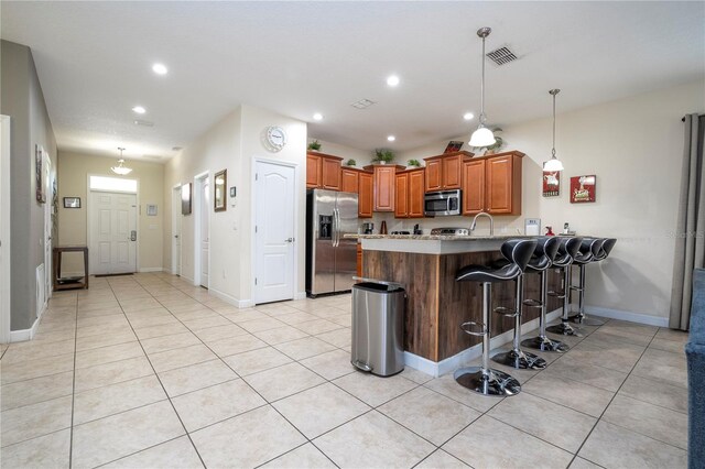 1439 Moon Valley Dr, Davenport, FL 33896 - kitchen with appliances with stainless steel finishes, a peninsula, brown cabinetry, light tile patterned floors, and a kitchen bar