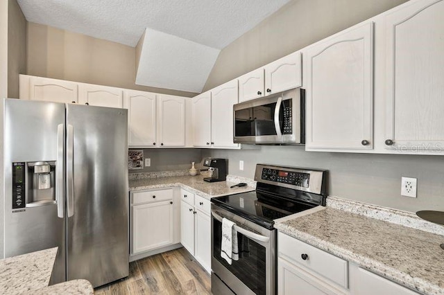 17516 Blessing Dr, Clermont, FL 34714 - kitchen with stainless steel appliances, white cabinets, light wood finished floors, light stone countertops, and vaulted ceiling