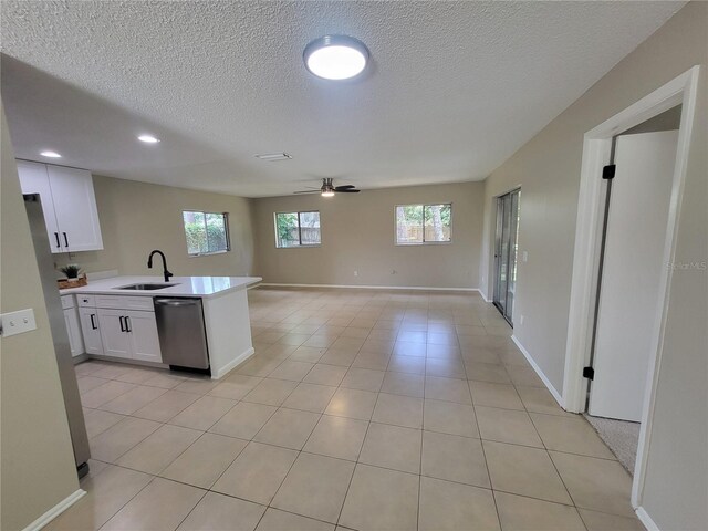 4883 Cherokee Rose Dr, Orlando, FL 32808 - kitchen with stainless steel dishwasher, white cabinetry, light countertops, healthy amount of natural light, and a textured ceiling