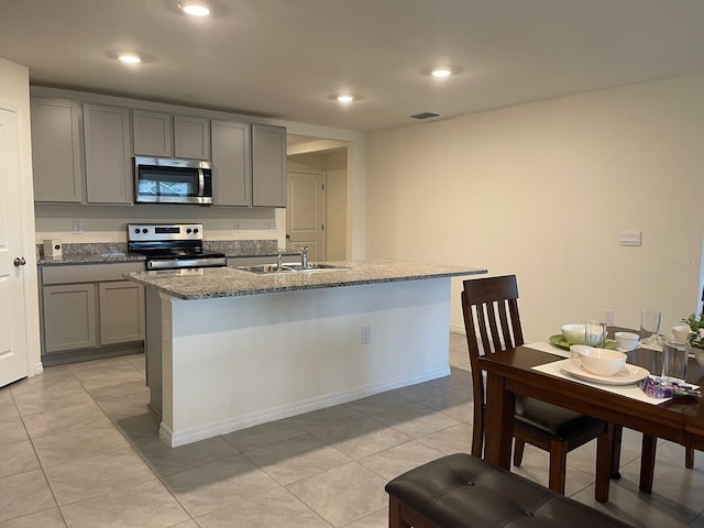 7172 SW 135th Pl, Ocala, FL 34473 - kitchen with stainless steel appliances, gray cabinets, stone countertops, light tile patterned floors, and a kitchen island with sink