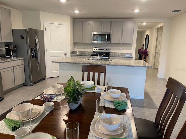 7172 SW 135th Pl, Ocala, FL 34473 - kitchen featuring stainless steel appliances, gray cabinetry, a center island with sink, light tile patterned floors, and light stone countertops