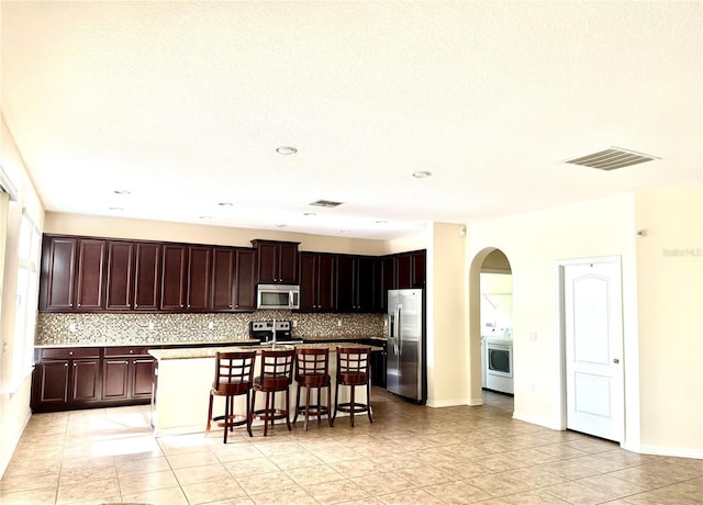 1016 Fountain Coin Loop, Orlando, FL 32828 - kitchen with appliances with stainless steel finishes, backsplash, a kitchen bar, arched walkways, and an island with sink