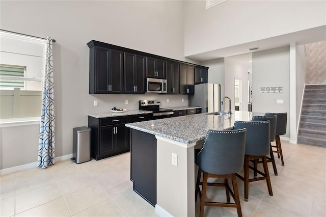 5639 Timber Meadow Way, Saint Cloud, FL 34771 - kitchen with appliances with stainless steel finishes, light tile patterned floors, dark cabinets, a center island with sink, and a high ceiling