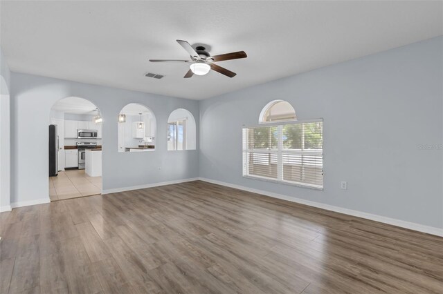 2255 Tealwood Cir, Tavares, FL 32778 - unfurnished living room with a ceiling fan, light wood-style flooring, baseboards, and arched walkways