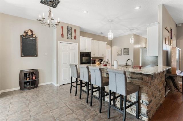 1031 Kings Hwy, Kissimmee, FL 34744 - kitchen featuring black oven, a kitchen bar, white cabinetry, a peninsula, and freestanding refrigerator