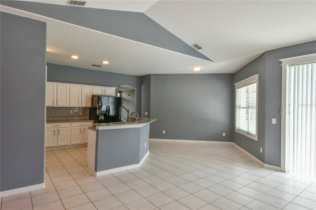 831 Corvina Dr, Davenport, FL 33897 - kitchen with black fridge with ice dispenser, lofted ceiling, decorative backsplash, arched walkways, and light tile patterned flooring