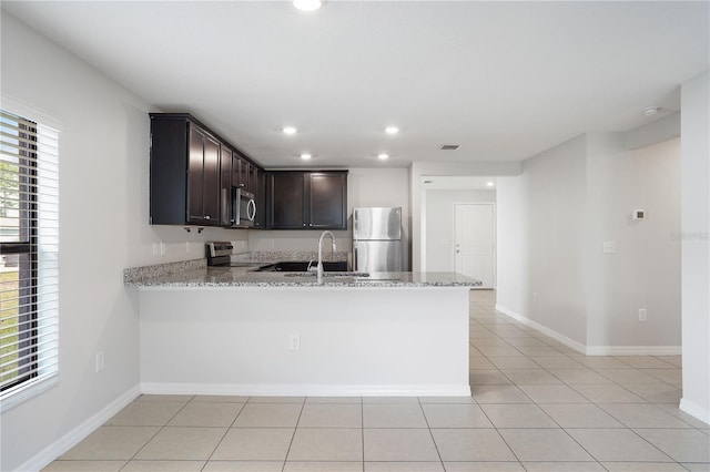 257 Fig Ct, Kissimmee, FL 34759 - kitchen with stainless steel appliances, light stone countertops, a peninsula, dark brown cabinetry, and light tile patterned floors