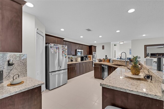 19367 NW 13th St, Pembroke Pines, FL 33029 - kitchen with appliances with stainless steel finishes, a sink, dark brown cabinets, backsplash, and light stone countertops