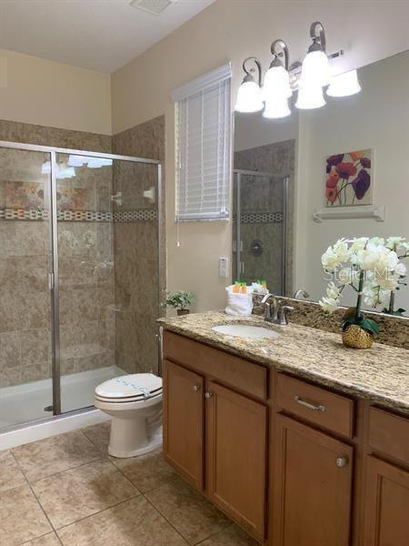 8894 Candy Palm Rd, Kissimmee, FL 34747 - full bathroom featuring a chandelier, vanity, toilet, a shower stall, and tile patterned floors