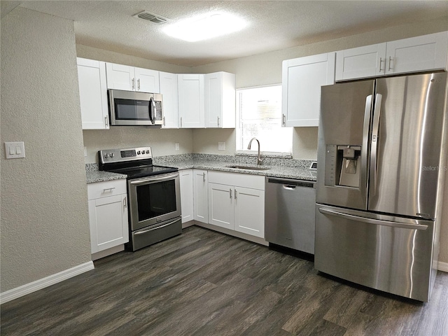 kitchen with stainless steel appliances, a sink, a textured wall, white cabinetry, and dark wood-type flooring