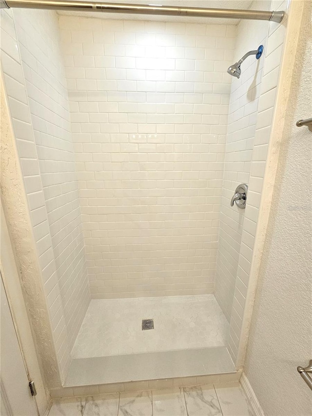 bathroom with marble finish floors, a shower stall, a textured wall, and baseboards