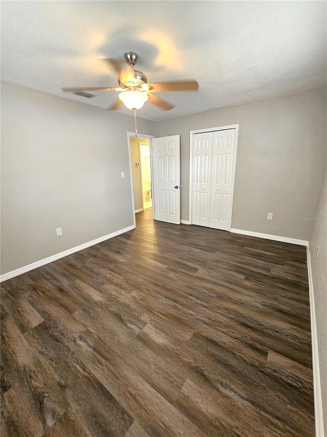 unfurnished bedroom featuring baseboards, dark wood-style flooring, a closet, and a ceiling fan