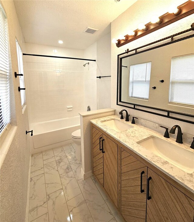 full bath featuring double vanity, washtub / shower combination, toilet, marble look tile flooring, and healthy amount of natural light