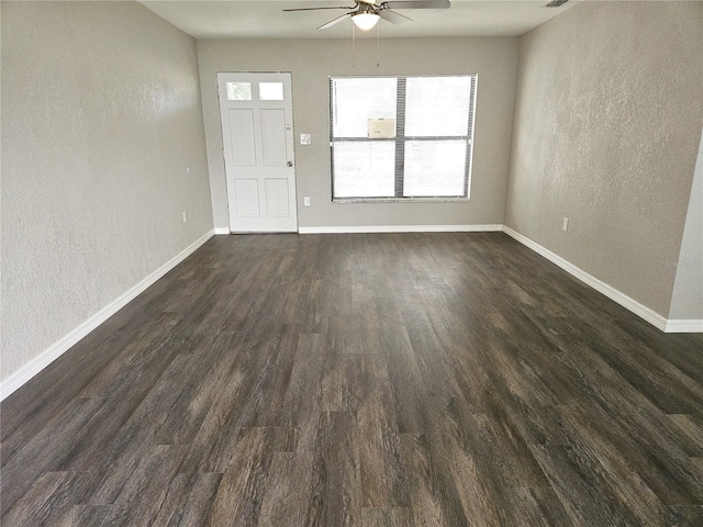 unfurnished living room featuring ceiling fan, dark wood-style flooring, a textured wall, and baseboards