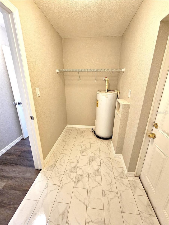 laundry area featuring water heater, a textured wall, a textured ceiling, and marble finish floors