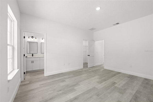 10290 N Biscayne Dr, Citrus Springs, FL 34434 - unfurnished bedroom featuring light wood finished floors, multiple windows, ensuite bathroom, a walk in closet, and recessed lighting