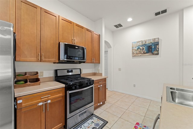 13768 Bluebird Pond Rd, Windermere, FL 34786 - kitchen with stainless steel appliances, arched walkways, light countertops, a sink, and brown cabinetry