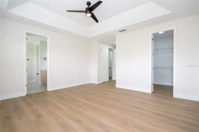 5161 Dove Tree St, Orlando, FL 32811 - unfurnished bedroom featuring a raised ceiling, light wood finished floors, a walk in closet, connected bathroom, and ceiling fan