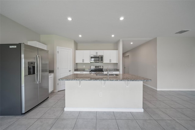 489 Panaro Ln, Haines City, FL 33844 - kitchen with appliances with stainless steel finishes, a sink, dark stone counters, a kitchen island with sink, and white cabinetry