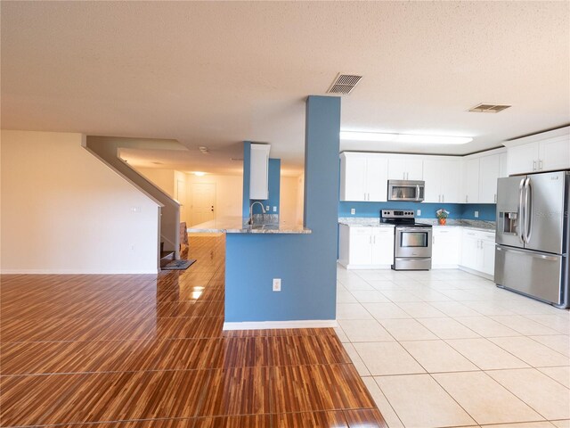 8330 Lainie Ln, Orlando, FL 32818 - kitchen featuring appliances with stainless steel finishes, light stone countertops, white cabinetry, a textured ceiling, and light tile patterned floors