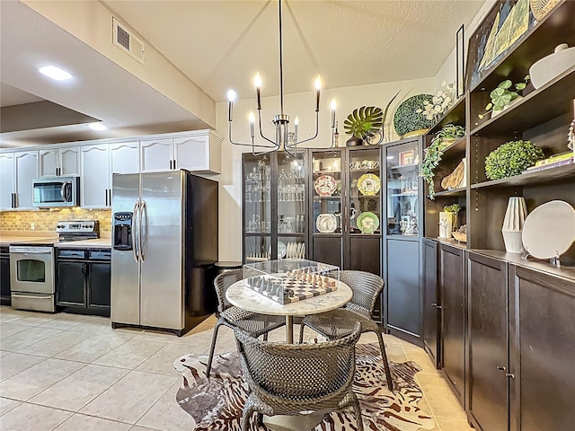 6336 Buford St Unit 207, Orlando, FL 32835 - kitchen with appliances with stainless steel finishes, light tile patterned floors, a chandelier, backsplash, and white cabinetry