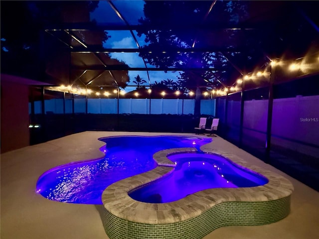 14723 Pine Cone Trl, Clermont, FL 34711 - pool at night featuring a fenced backyard, a patio, a pool with connected hot tub, and a lanai
