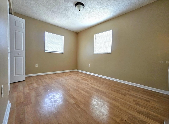 empty room with light wood-style flooring, a textured ceiling, and baseboards