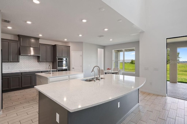 1551 Gateway Ln, Kissimmee, FL 34746 - kitchen featuring a kitchen island with sink, under cabinet range hood, wood finish floors, tasteful backsplash, and recessed lighting