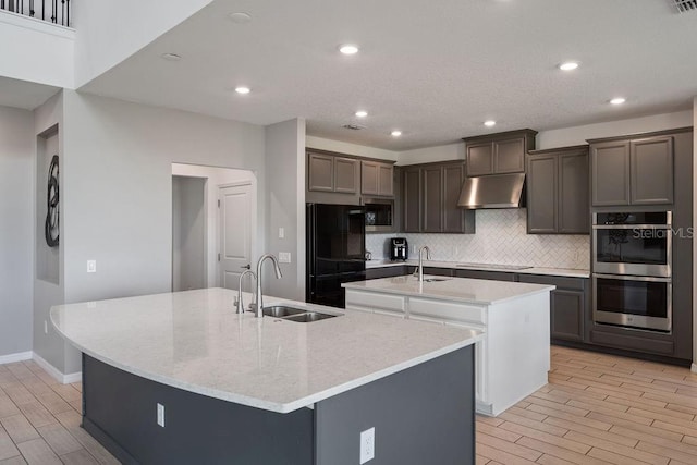 1551 Gateway Ln, Kissimmee, FL 34746 - kitchen with a center island with sink, under cabinet range hood, appliances with stainless steel finishes, tasteful backsplash, and light wood finished floors