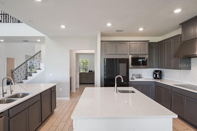 1551 Gateway Ln, Kissimmee, FL 34746 - kitchen with black appliances, under cabinet range hood, an island with sink, decorative backsplash, and light stone counters