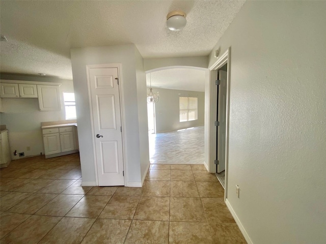 1524 Conway Ct, The Villages, FL 32162 - corridor with arched walkways, healthy amount of natural light, a textured ceiling, light tile patterned floors, and baseboards