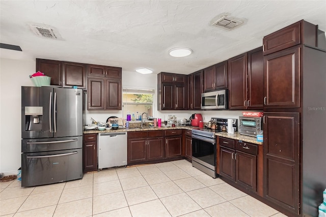 3280 Pinto Dr, Kissimmee, FL 34746 - kitchen featuring stainless steel appliances, light tile patterned floors, light stone counters, and dark brown cabinetry