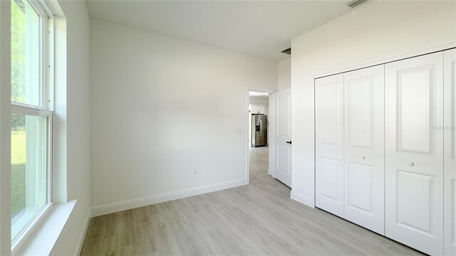 2498 W Magenta Dr, Citrus Springs, FL 34434 - unfurnished bedroom featuring stainless steel fridge with ice dispenser, light wood-type flooring, multiple windows, and a closet