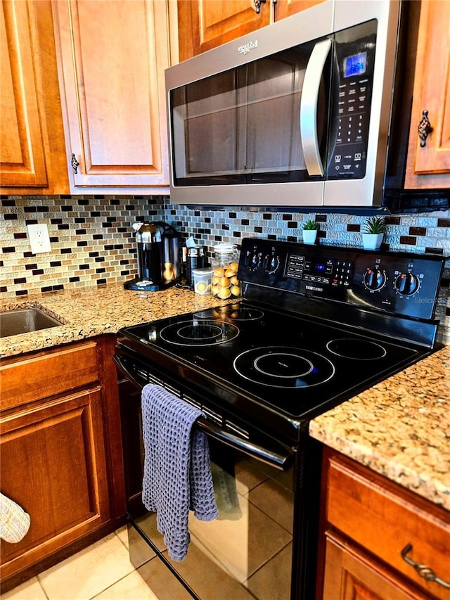 2947 S Atlantic Ave Unit 601, Daytona Beach, FL 32118 - kitchen with black range with electric cooktop, stainless steel microwave, light tile patterned flooring, backsplash, and light stone countertops