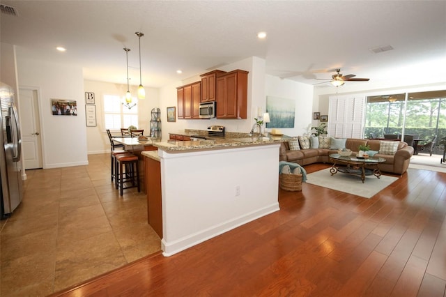 3574 La Jolla Dr, Clermont, FL 34711 - kitchen featuring brown cabinetry, light stone counters, stainless steel appliances, healthy amount of natural light, and recessed lighting