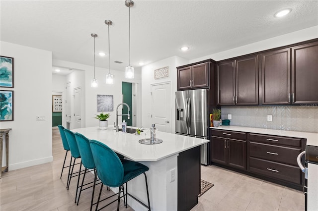 363 Miro Dr, Davenport, FL 33837 - kitchen with stainless steel fridge, light countertops, a kitchen bar, dark brown cabinets, and an island with sink
