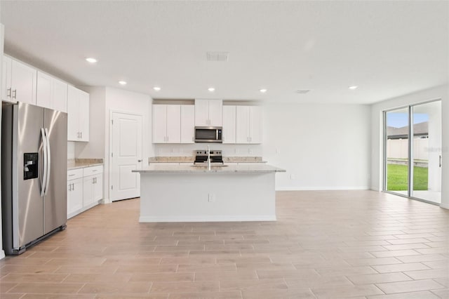 1732 Brekey Way, Zephyrhills, FL 33541 - kitchen featuring appliances with stainless steel finishes, white cabinets, recessed lighting, a center island with sink, and light stone countertops