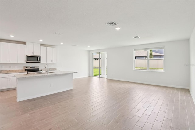 1732 Brekey Way, Zephyrhills, FL 33541 - kitchen with stainless steel appliances, open floor plan, white cabinetry, a kitchen island with sink, and light wood finished floors