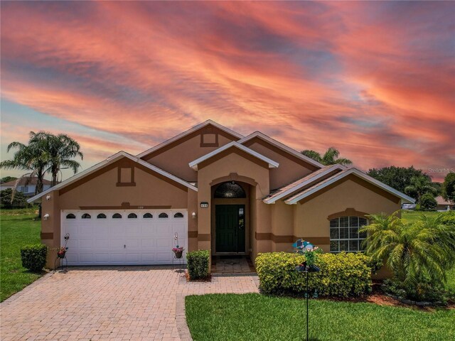 456 Old Bridge Cir, Davenport, FL 33897 - view of front of house featuring stucco siding, an attached garage, decorative driveway, and a lawn