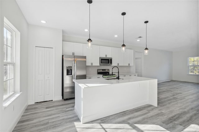 3159 SW 127th Lane Rd, Ocala, FL 34473 - kitchen featuring appliances with stainless steel finishes, white cabinets, light countertops, a center island with sink, and decorative light fixtures