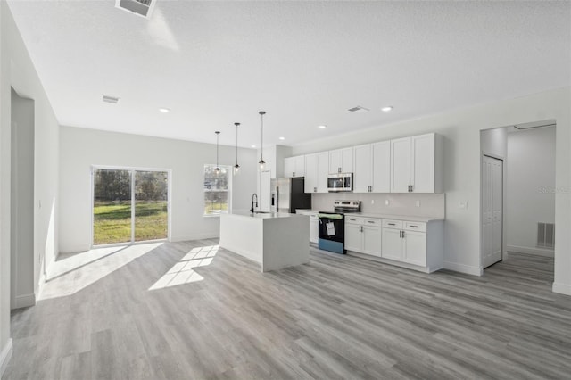 3159 SW 127th Lane Rd, Ocala, FL 34473 - kitchen featuring stainless steel appliances, light wood finished floors, a center island with sink, white cabinets, and light countertops