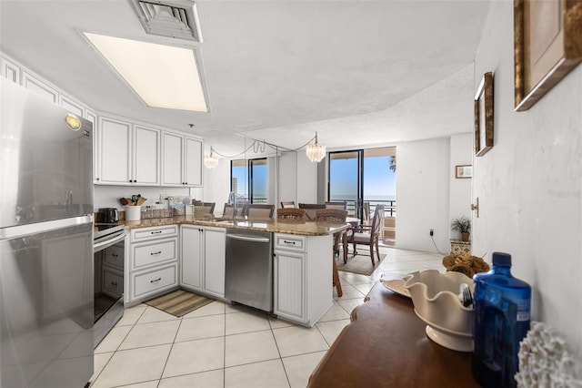 3023 S Atlantic Ave Unit 2050, Daytona Beach, FL 32118 - kitchen featuring stainless steel appliances, a peninsula, light tile patterned floors, white cabinetry, and stone countertops