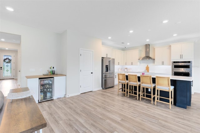 5677 Cedar Chase Dr, Saint Cloud, FL 34771 - kitchen featuring appliances with stainless steel finishes, wine cooler, wall chimney range hood, light wood finished floors, and a kitchen island with sink