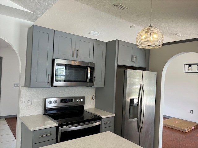 2421 Queenswood Cir, Kissimmee, FL 34743 - kitchen featuring stainless steel appliances, arched walkways, gray cabinets, pendant lighting, and a textured ceiling