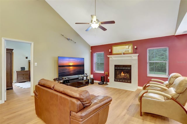 living area with light wood-style flooring, high vaulted ceiling, a ceiling fan, and a fireplace with flush hearth