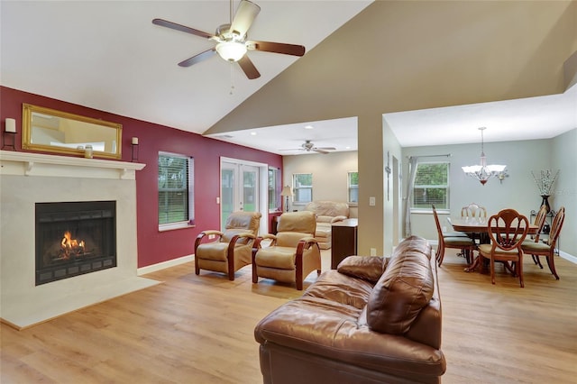 living room with ceiling fan, light wood-style flooring, a high end fireplace, a chandelier, and high vaulted ceiling