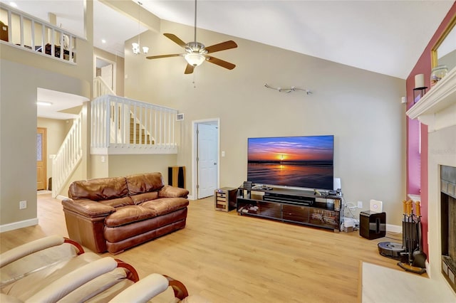 living room with high vaulted ceiling, stairs, a fireplace with flush hearth, wood finished floors, and a ceiling fan