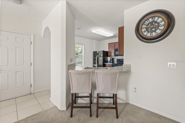 3537 Seneca Club Loop Unit B, Orlando, FL 32808 - kitchen featuring black appliances, baseboards, a kitchen bar, light countertops, and light carpet